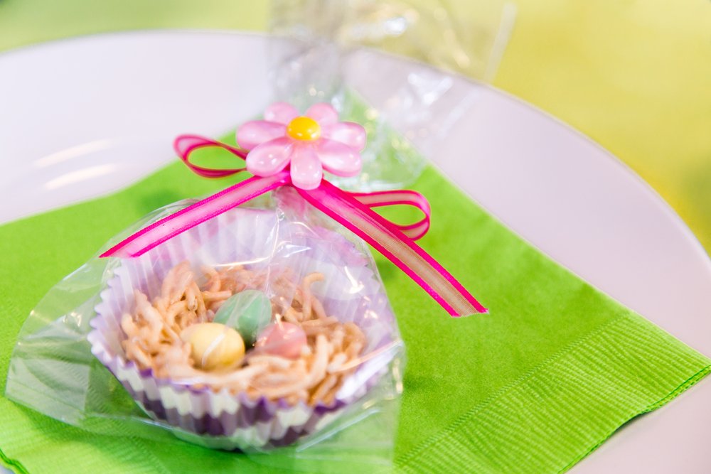 fun easter treat nest made with dry cereal and candy robins eggs wrapped in celophane and tied with a pink ribbon and pink flower decoration. Sitting on a green napkin and white plate