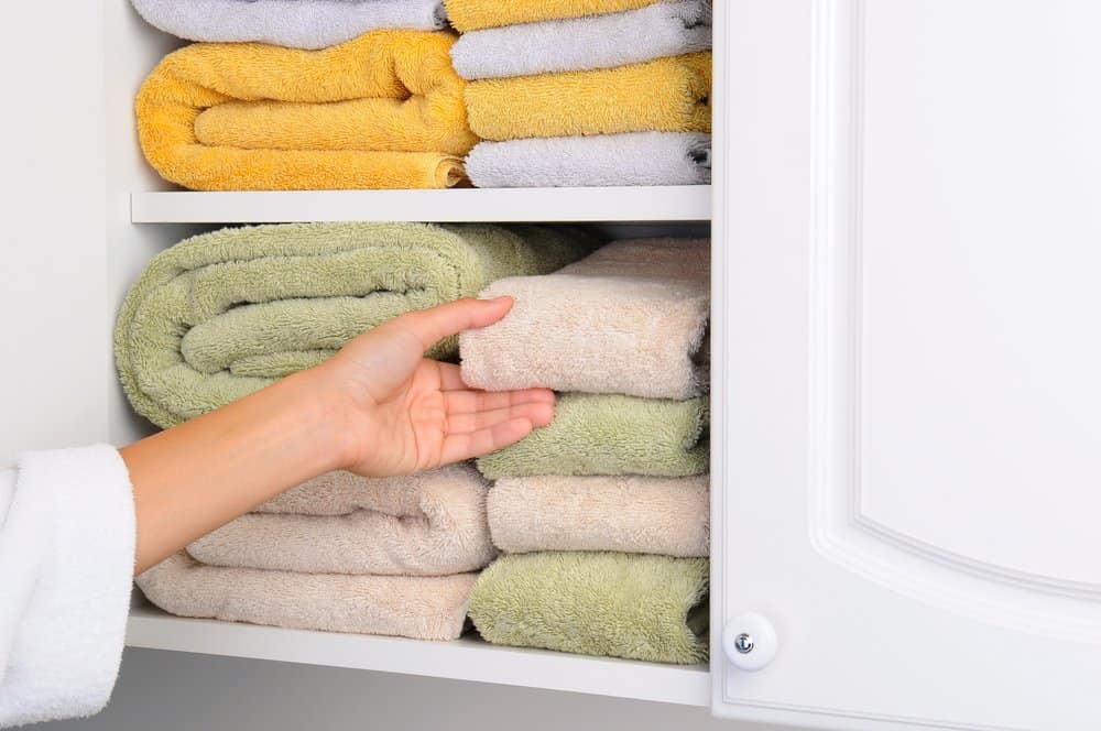 well organized towels in the colors of yellow green and tan stacked horizontally in a white bathroom cabinets