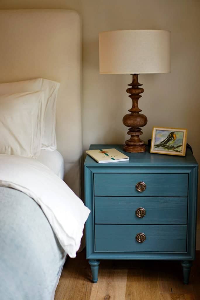 teal organized nightstand with brown light base a photograph, and notebook next to a bed