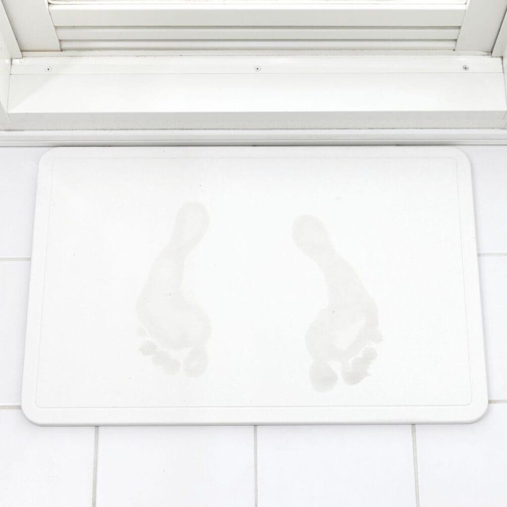 white bath mat on white tile floor with gray foot prints