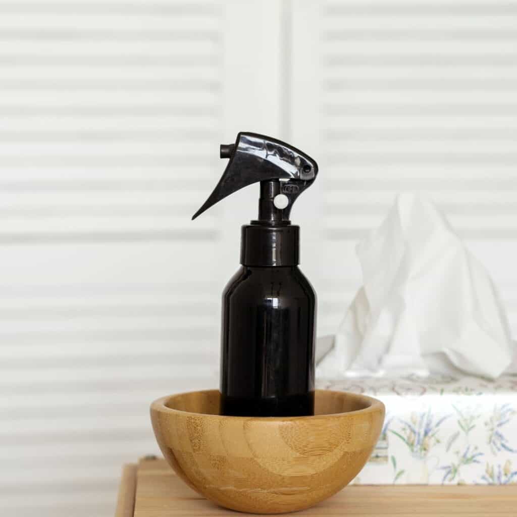 dark amber glass spray bottle with black sprayer sitting in a bowl next to a box of facial tissues